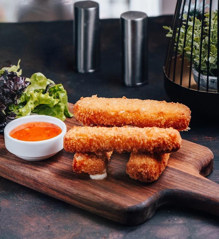 A wooden cutting board with fried cheese sticks and a bowl of sauce