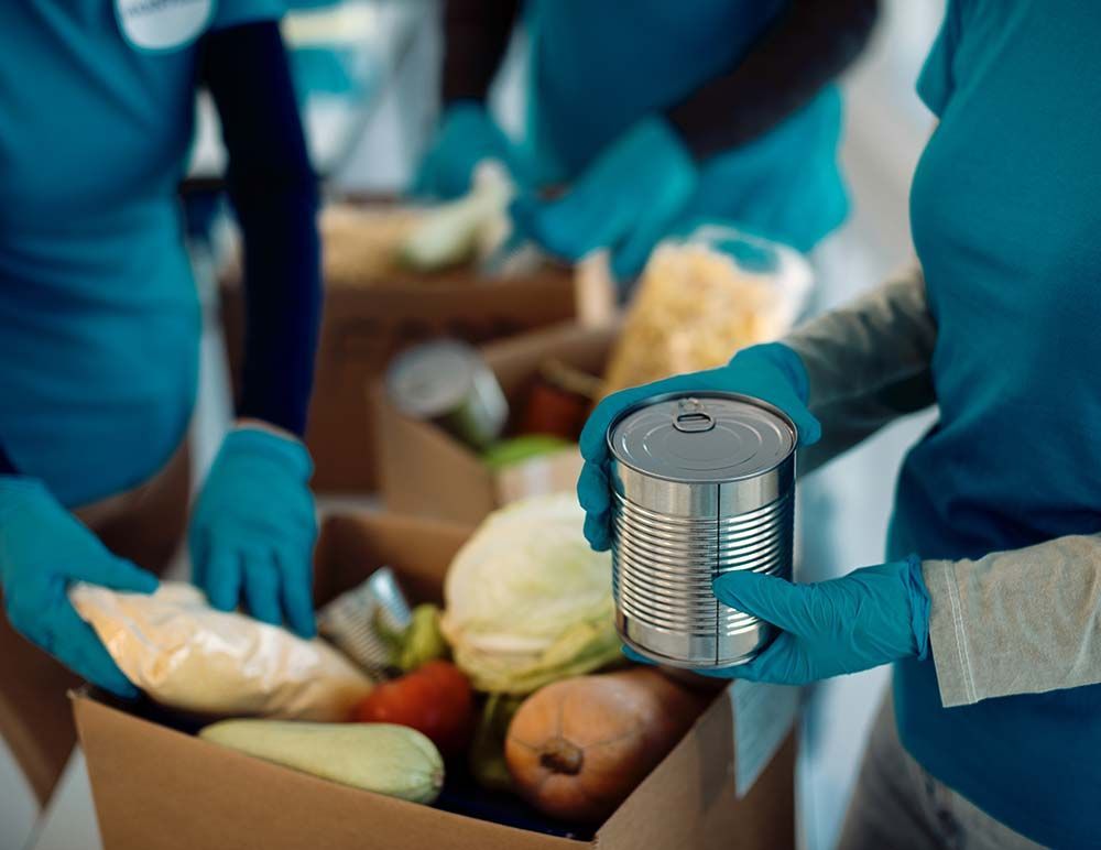 A group of people wearing blue gloves are putting vegetables in a box.