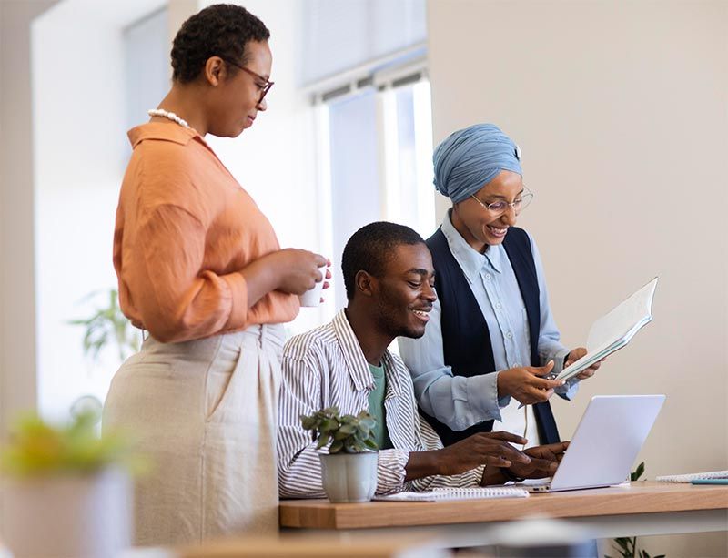 A group of people are standing around a table looking at a laptop.