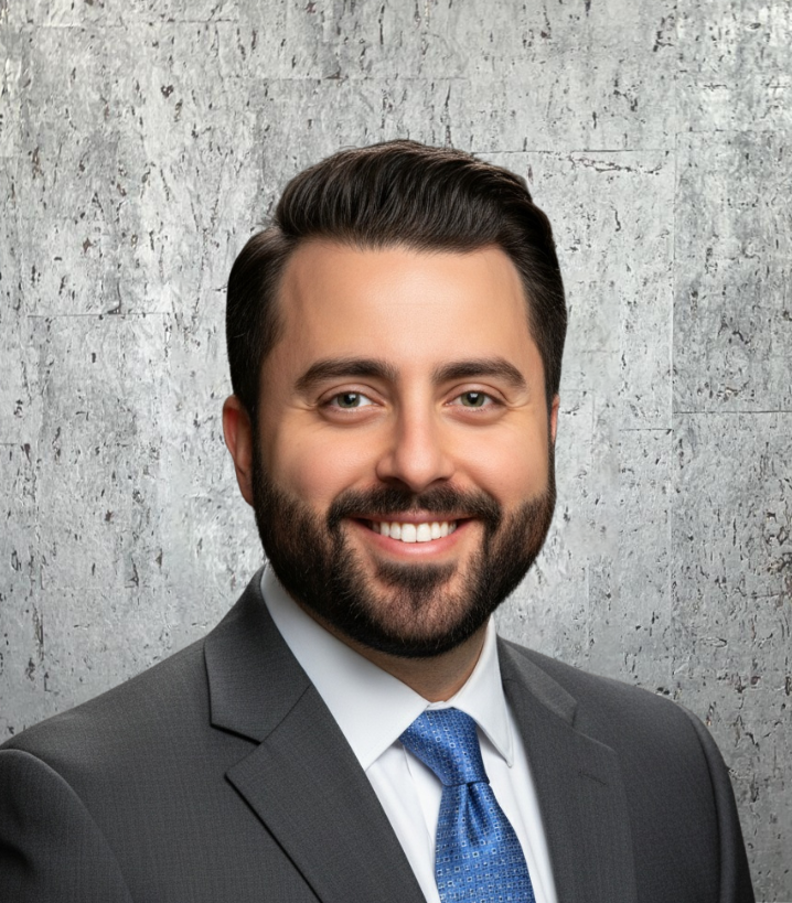 A man in a suit and tie stands in front of a concrete wall
