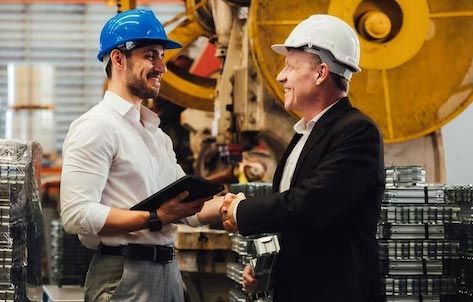 Two men in hard hats are shaking hands in a factory.