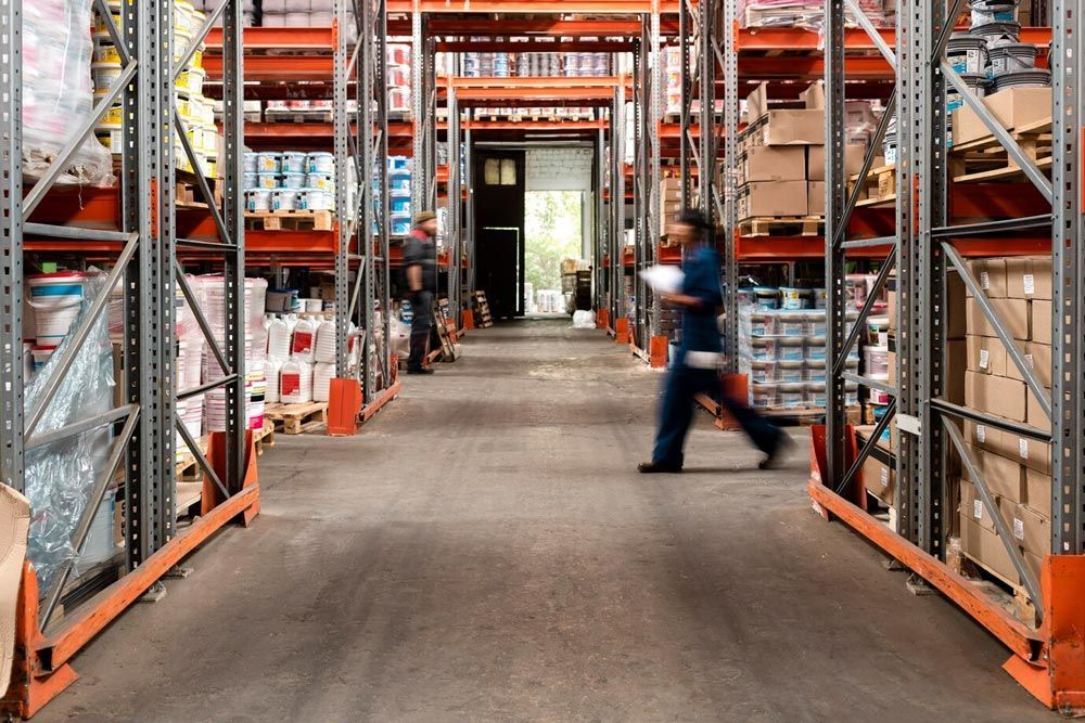 A man is walking through a warehouse filled with shelves and boxes.