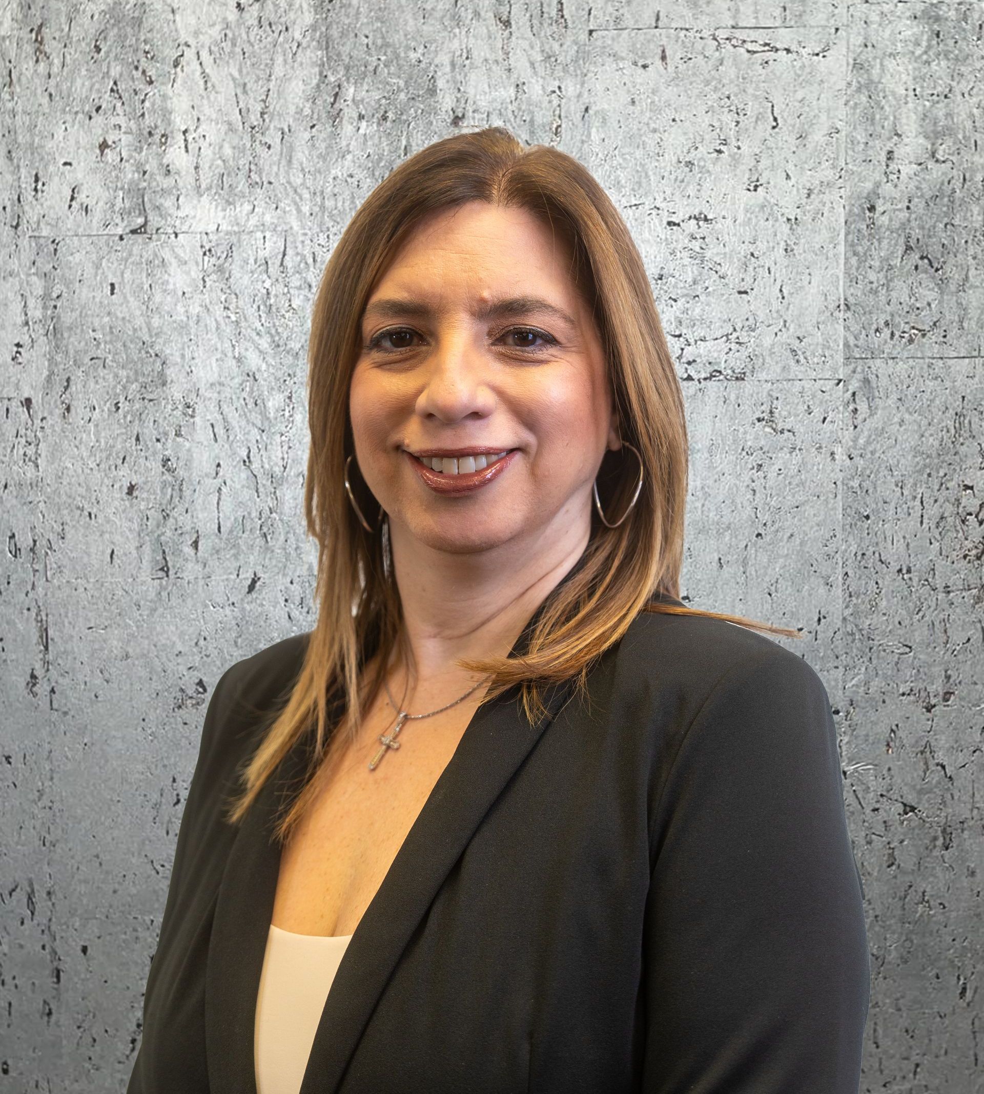 A woman in a suit is smiling in front of a concrete wall.