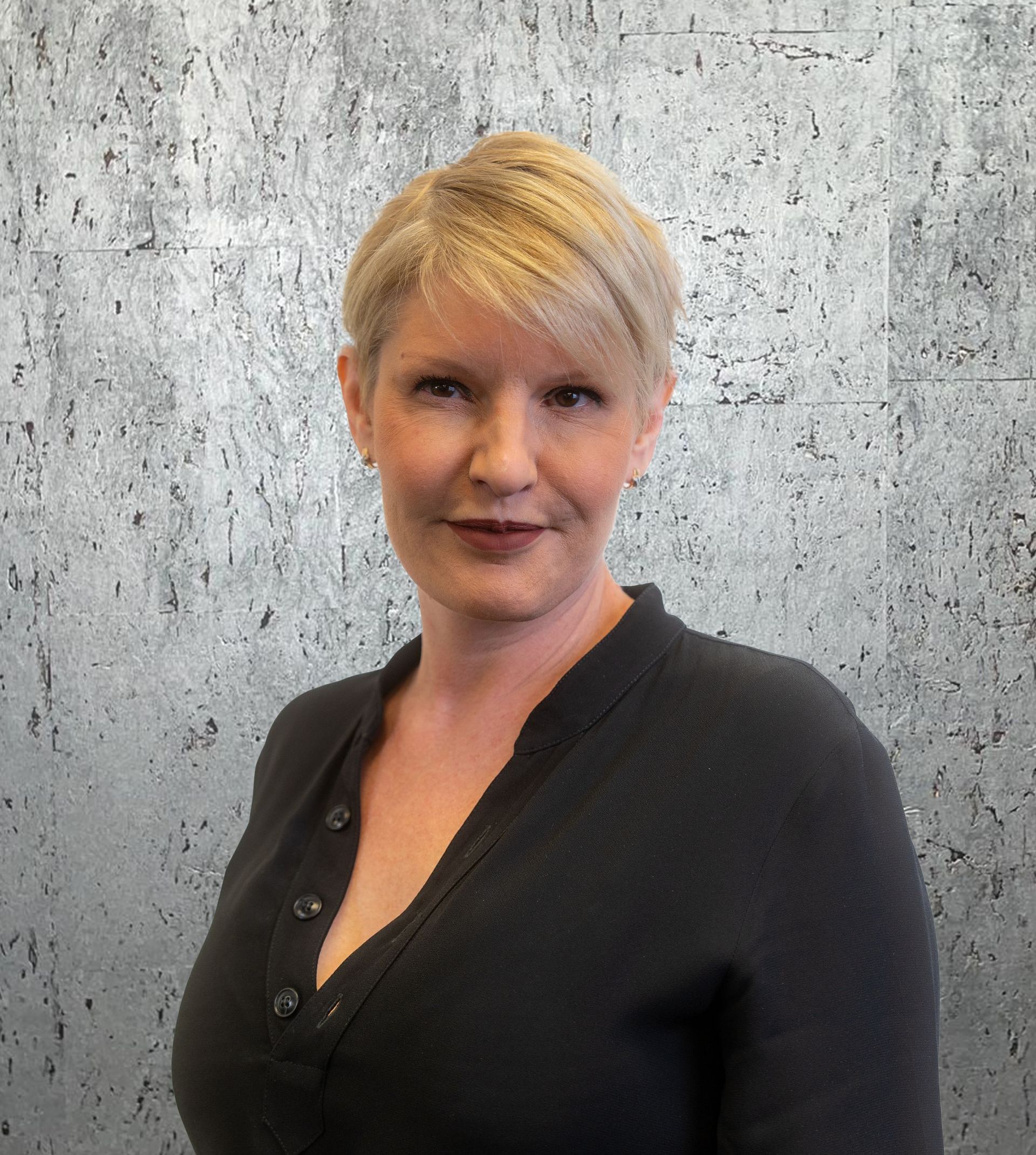 A woman in a black sweater is standing in front of a concrete wall.