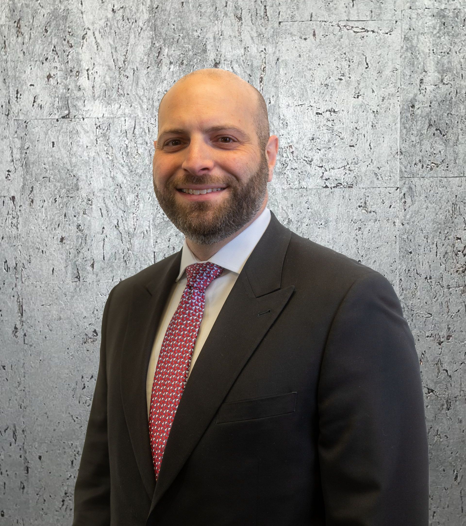 A man in a suit and tie is smiling in front of a concrete wall.