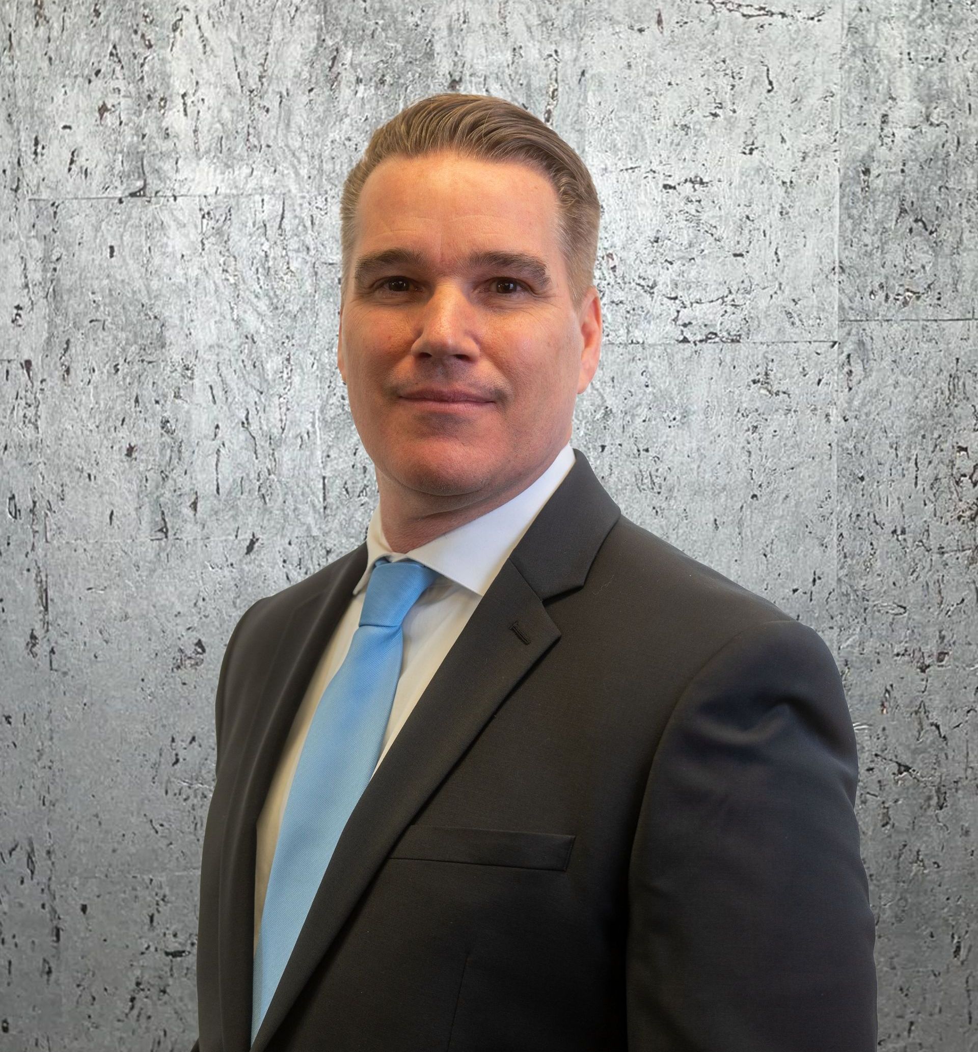 A man in a suit and tie is standing in front of a concrete wall.