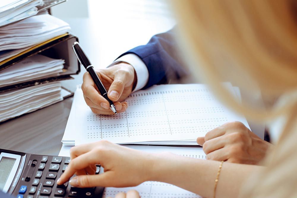 A woman is using a calculator while a man is writing on a piece of paper.