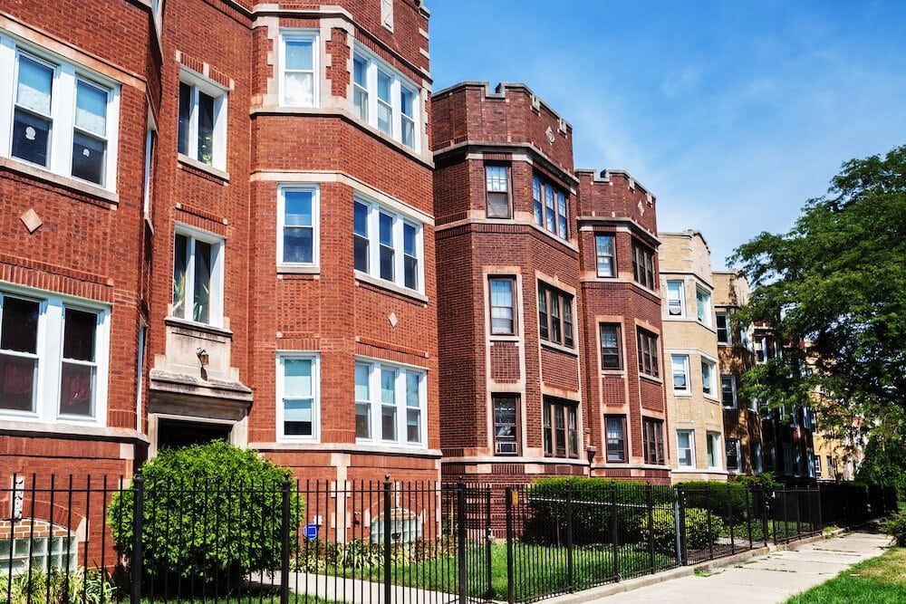 A row of brick apartment buildings with a fence in front of them.
