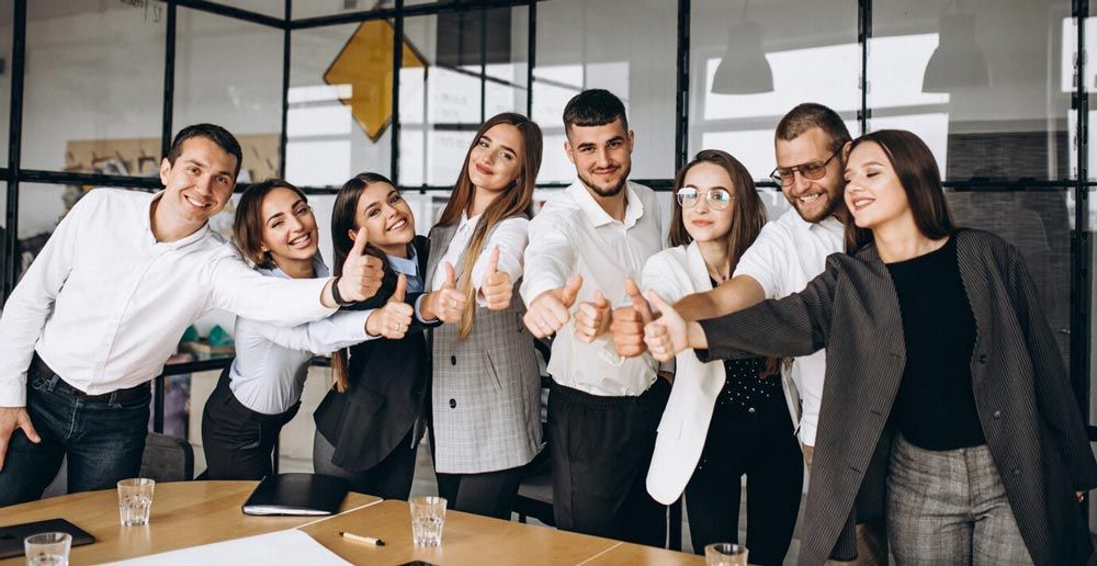 A group of people are standing around a table giving a thumbs up.