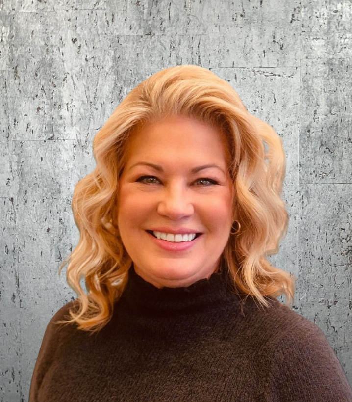 A woman in a black sweater is smiling in front of a concrete wall.