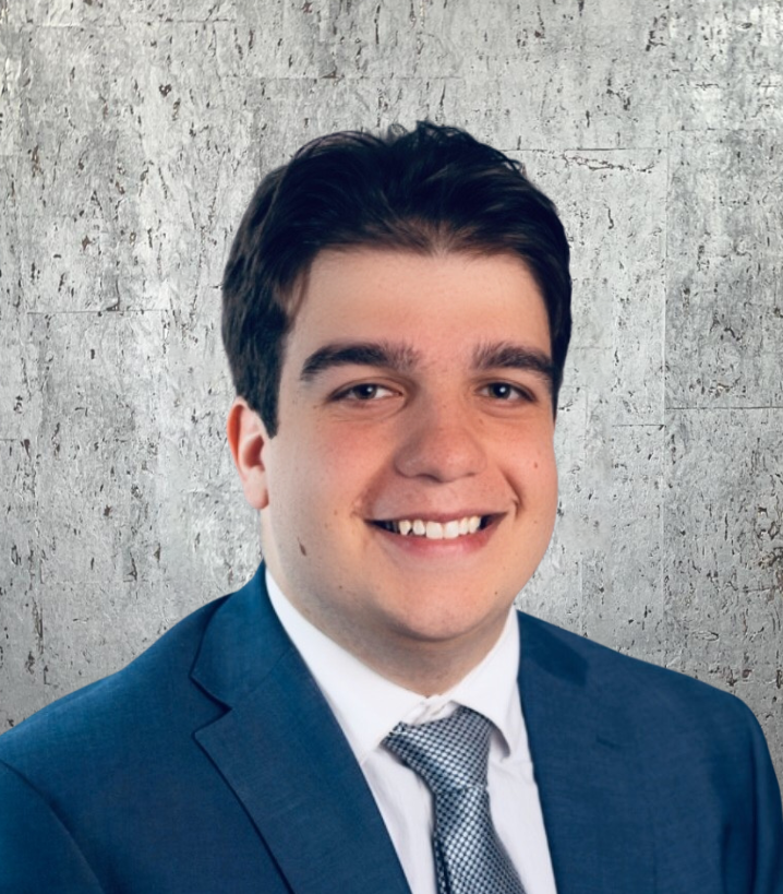 Man in a blue suit smiles at the camera, against a textured gray background.