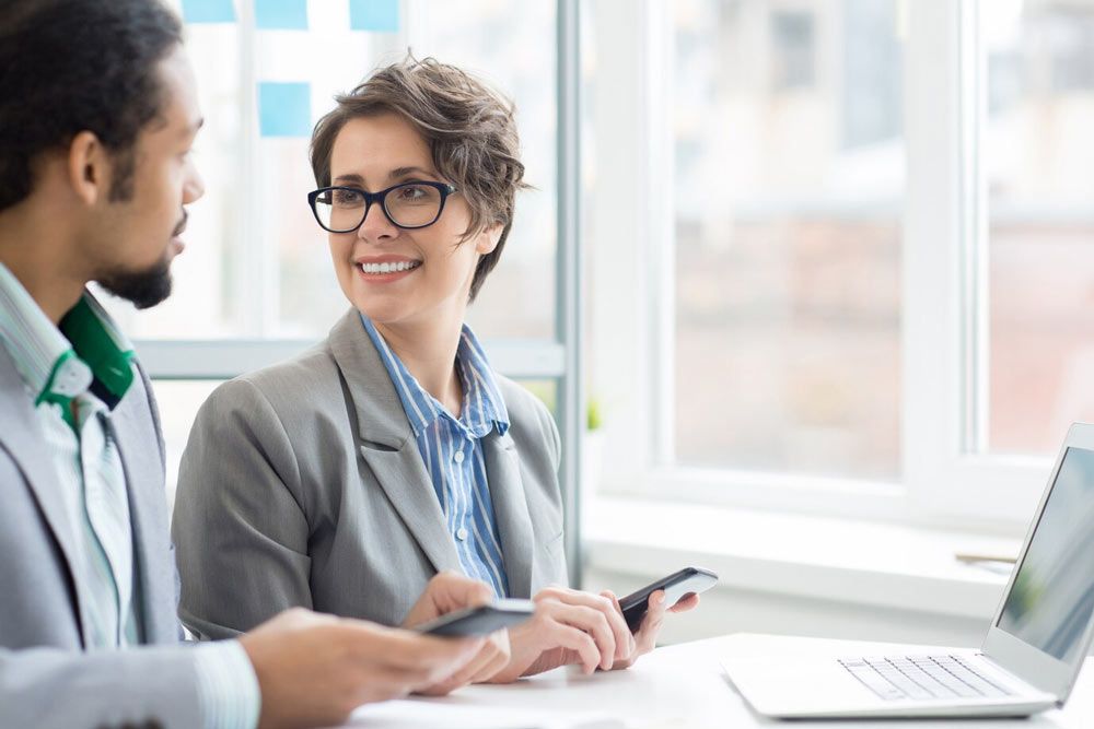 A man and a woman are sitting at a table with a laptop and a cell phone.