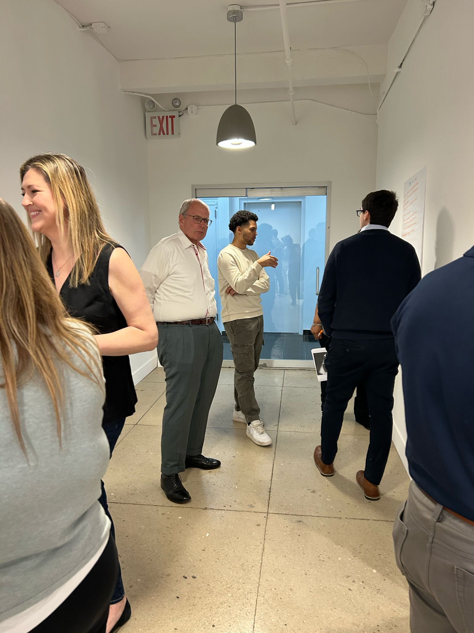 A group of people are standing in a room with an exit sign on the wall.