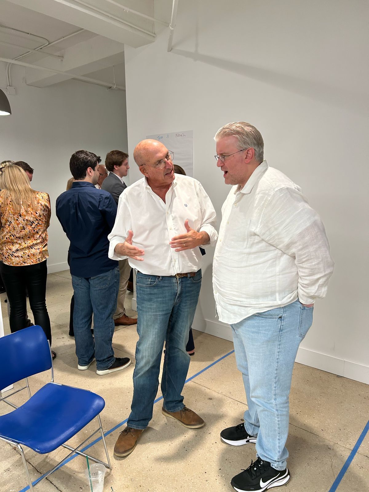 Two men are standing next to each other in a room talking to each other.