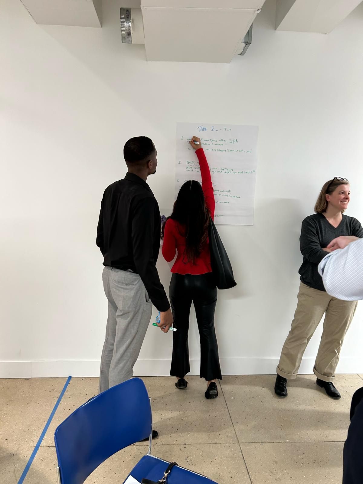 A woman is writing on a white board while standing next to a man and a woman.