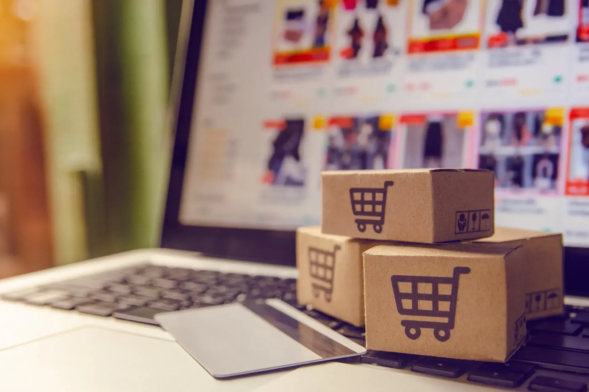 Three cardboard boxes with shopping carts on them are sitting on top of a laptop computer.