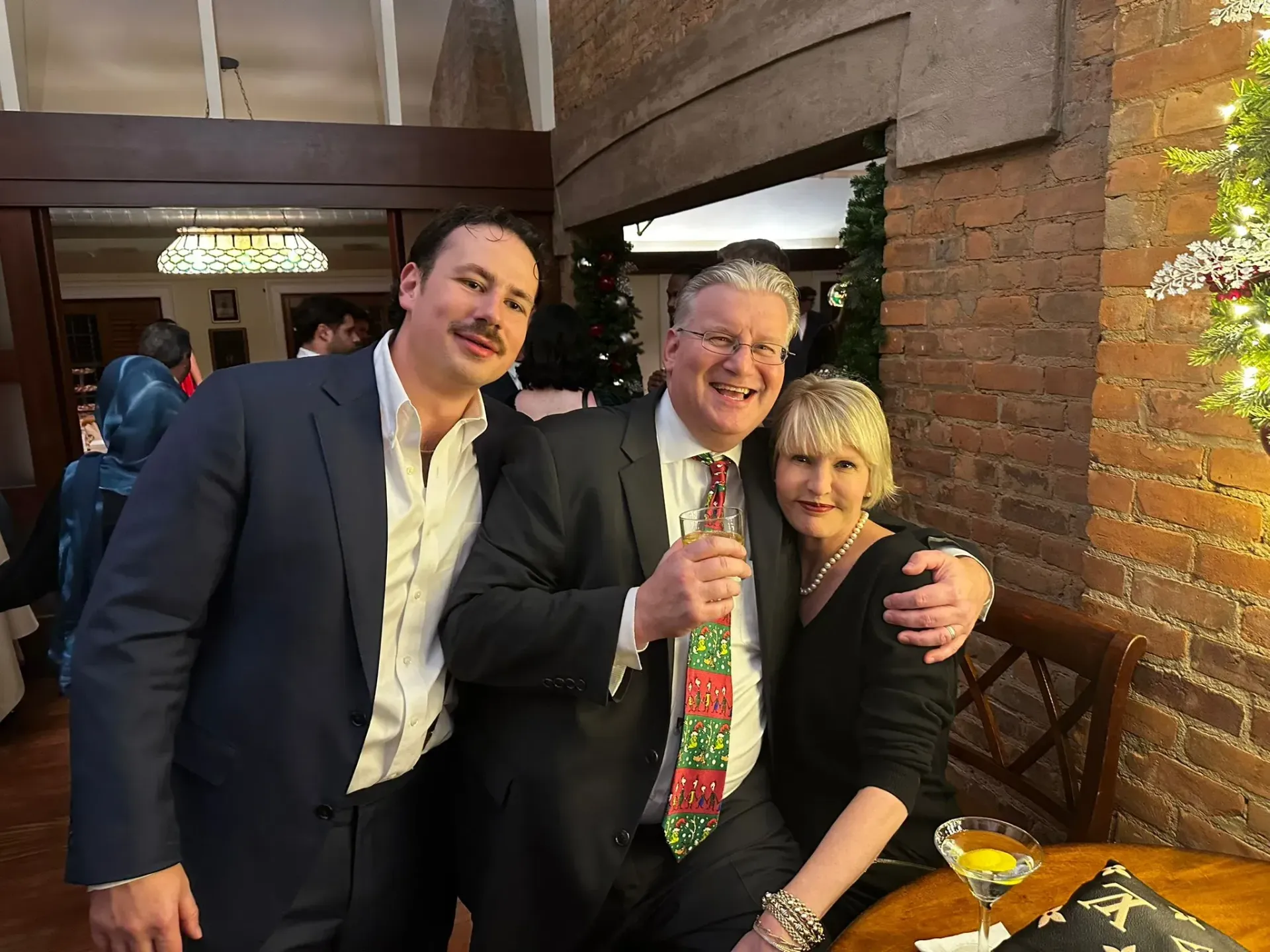 A man in a suit is standing next to a woman and a man in a tie.