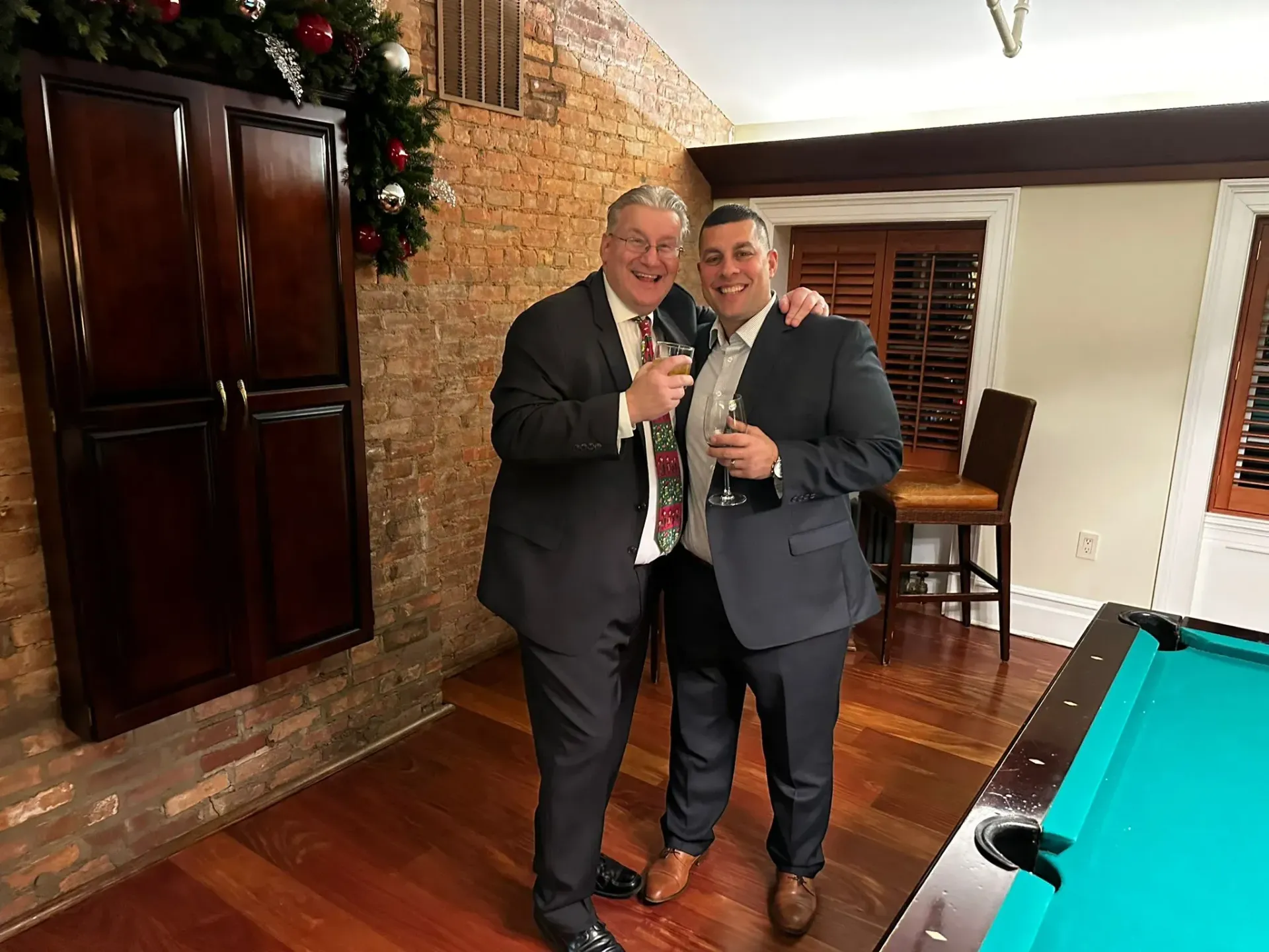 Two men in suits are standing next to each other in front of a pool table.