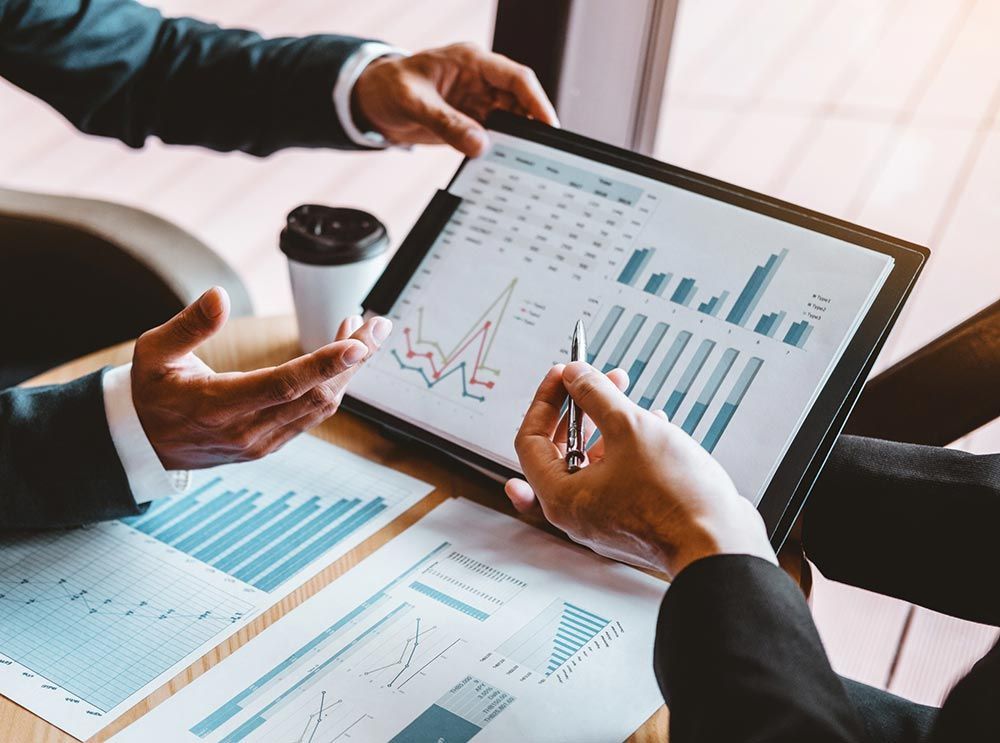 A man and a woman are looking at a tablet with graphs on it.