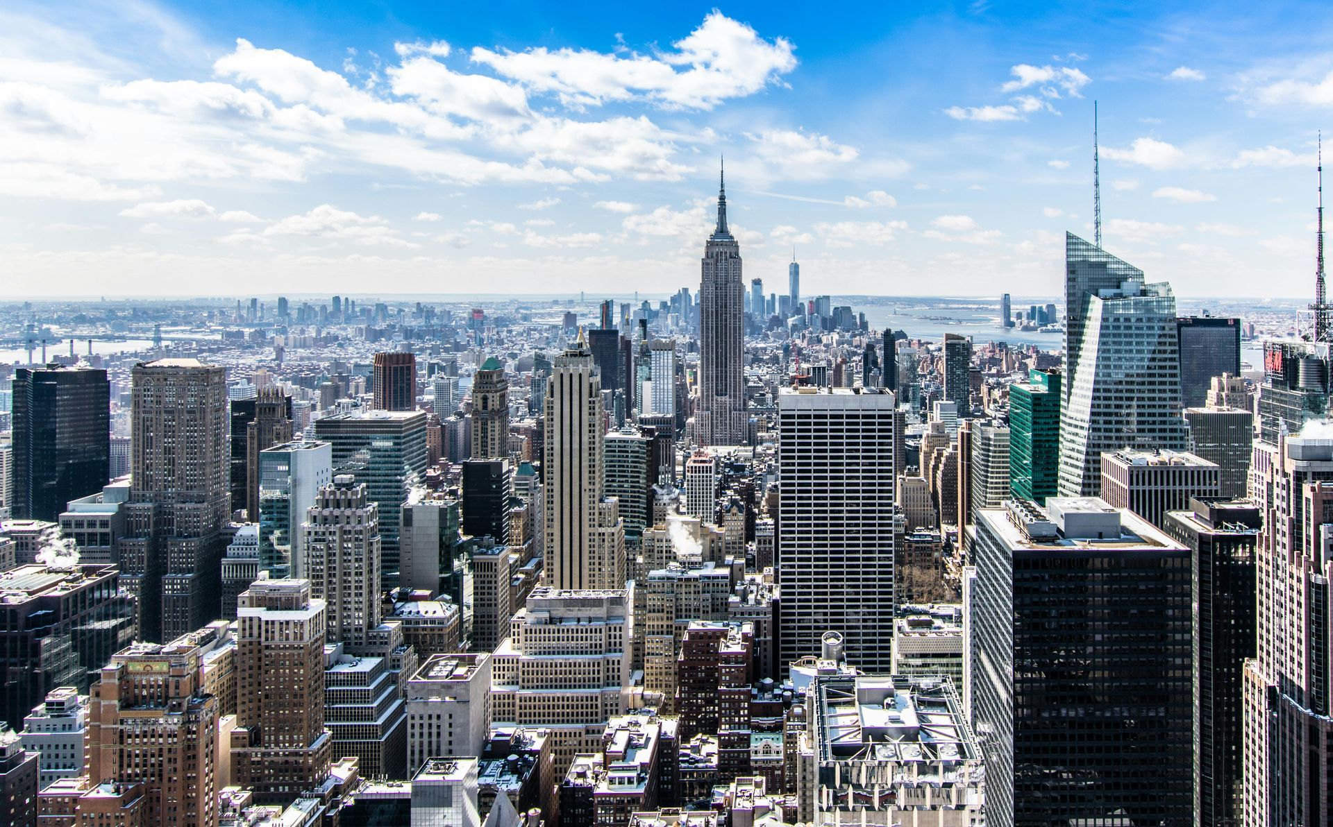 New York City skyline on a sunny day, with many tall buildings and a bright blue sky.