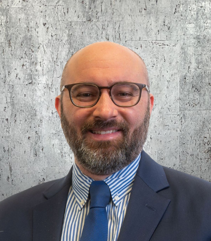 A bald man with a beard and glasses is wearing a suit and tie.