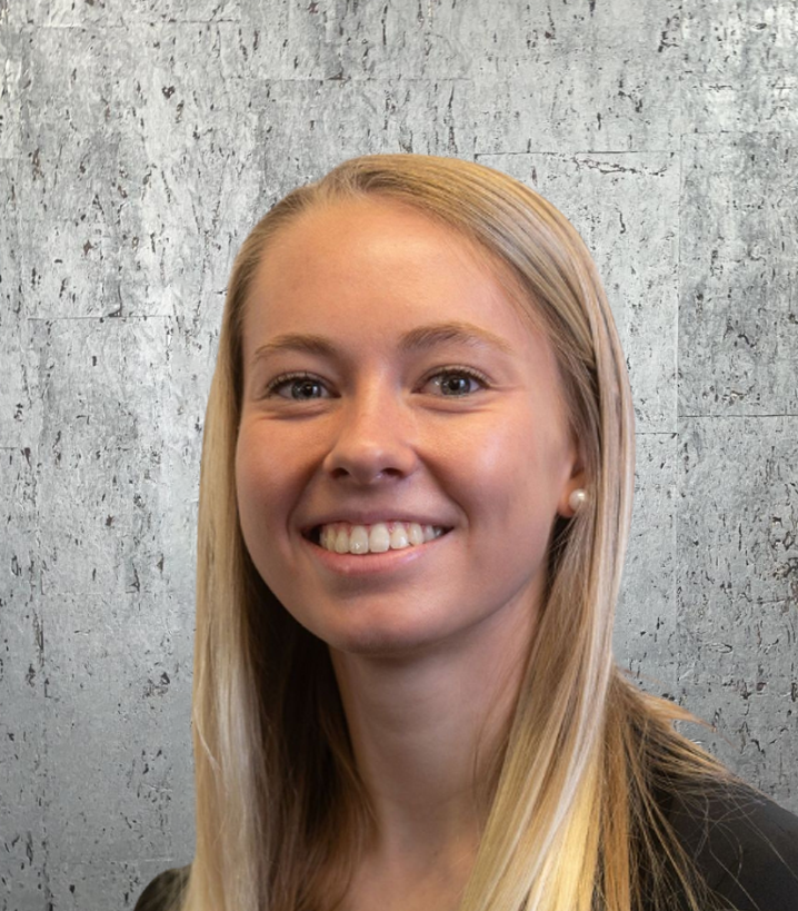 A woman with long blonde hair is smiling in front of a concrete wall.