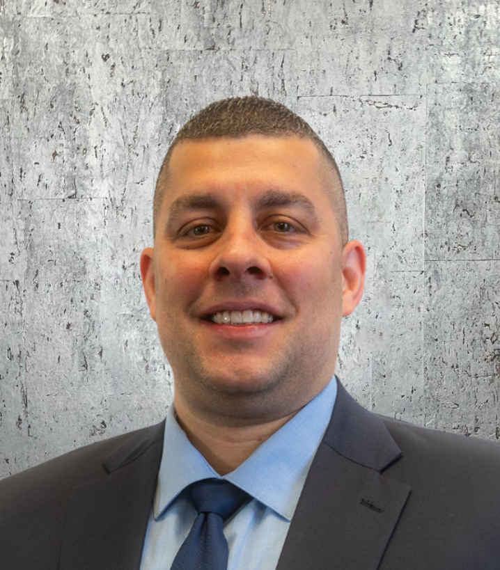 A man in a suit and tie is smiling in front of a concrete wall.