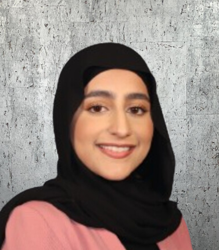 A woman wearing a black hijab and a pink shirt is smiling.