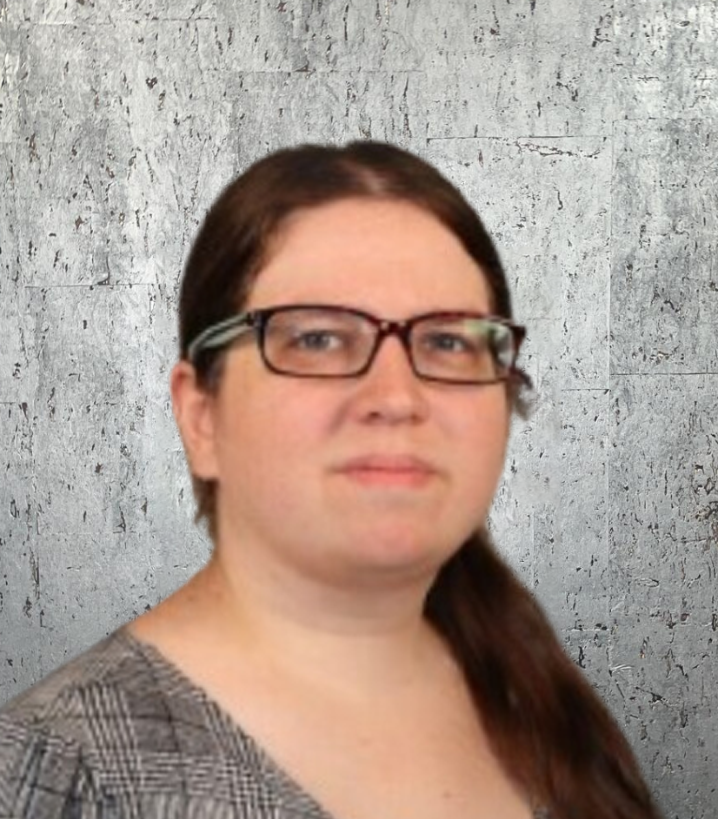 A woman wearing glasses and a plaid shirt is standing in front of a wall.