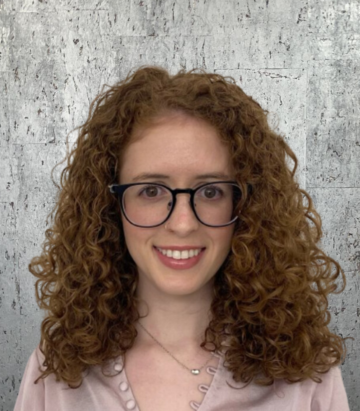 A woman with curly hair wearing glasses and a pink shirt