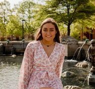 A woman in a pink dress is sitting in front of a water fountain.