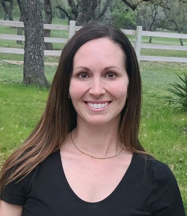 A woman in a black shirt is smiling in front of a white fence.