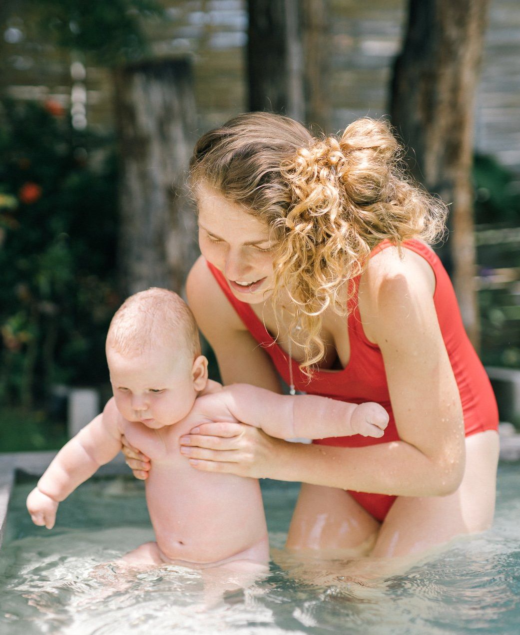 A woman in a red swimsuit is holding a baby in a pool.