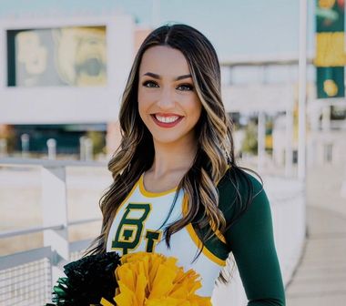 A cheerleader is wearing a green and white uniform and holding a pom pom.