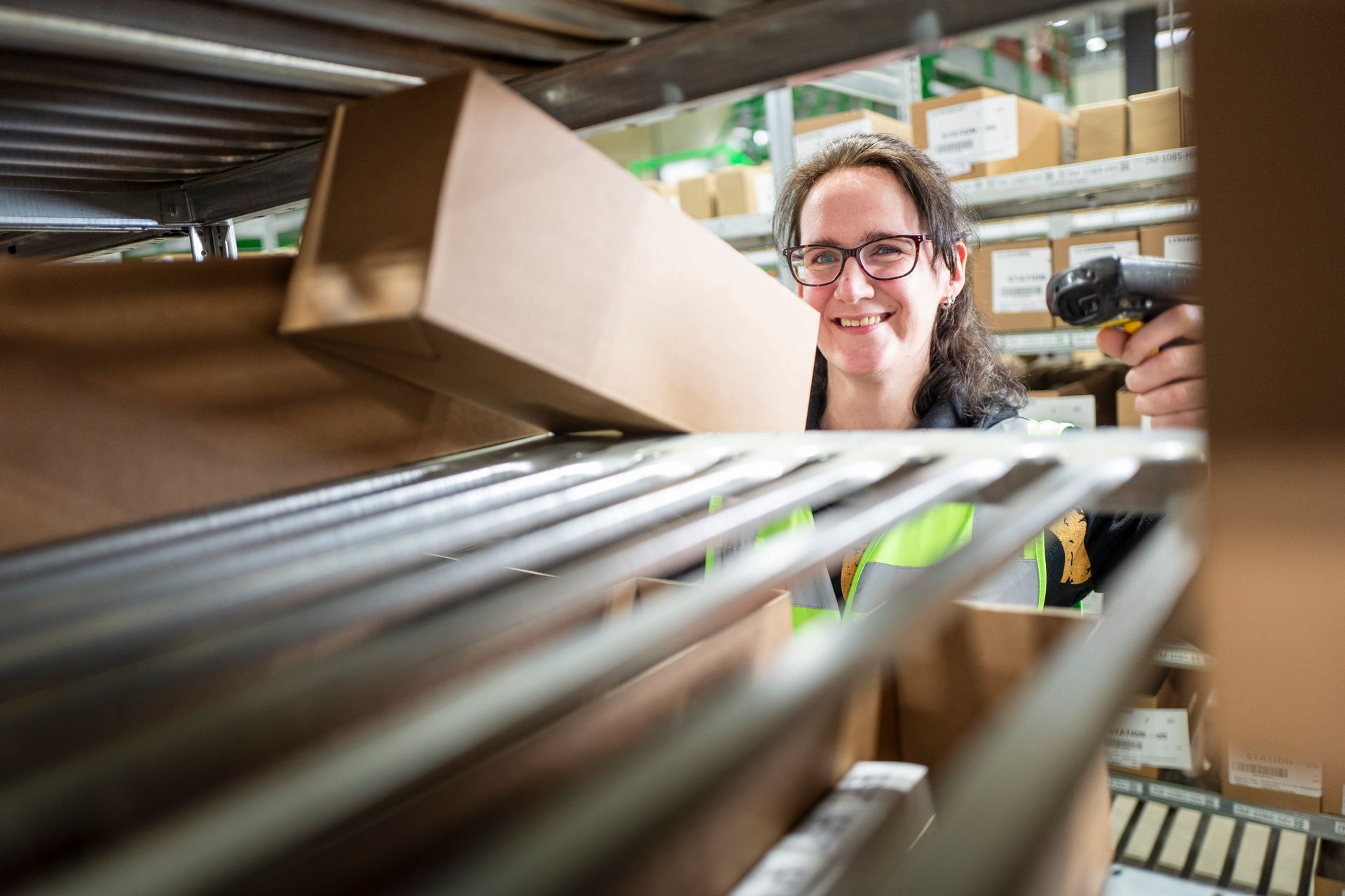 Een persoon scant een doos in een magazijn; op de achtergrond zijn schappen met dozen te zien.