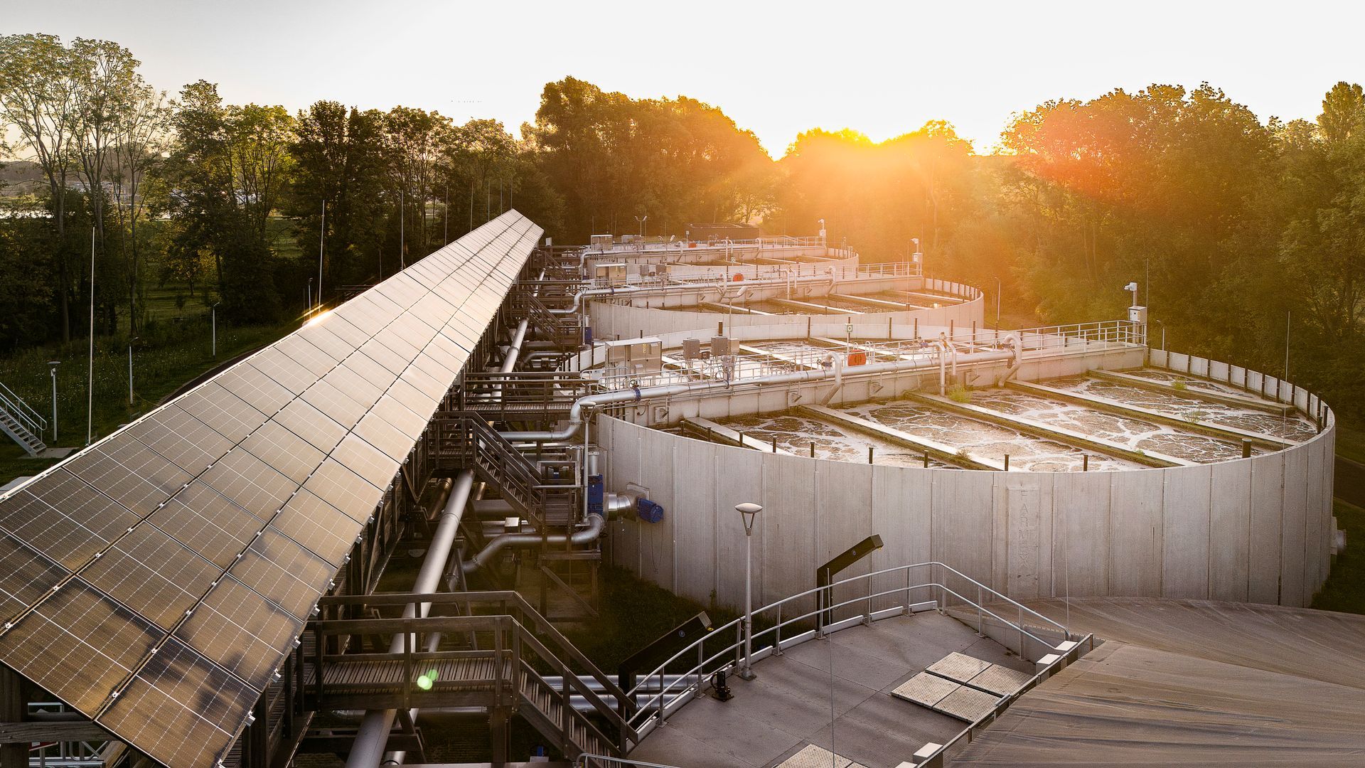 Zonnepanelen en waterzuiveringstanks baden in het licht van de opgaande zon.