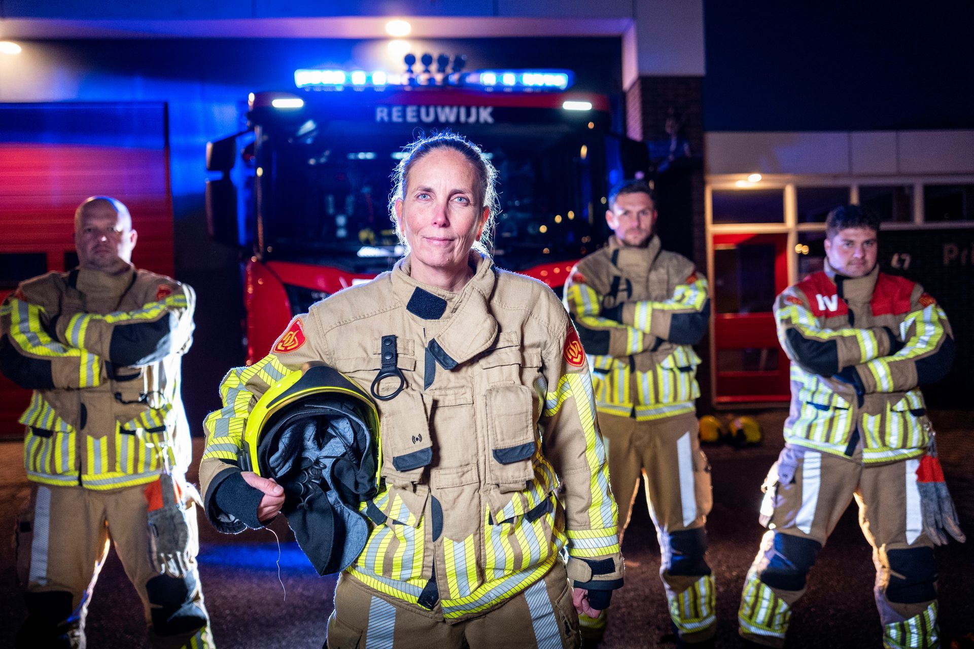 Brandweerlieden in uniform poseren voor een brandweerwagen bij een kazerne in Reeuwijk in de avond