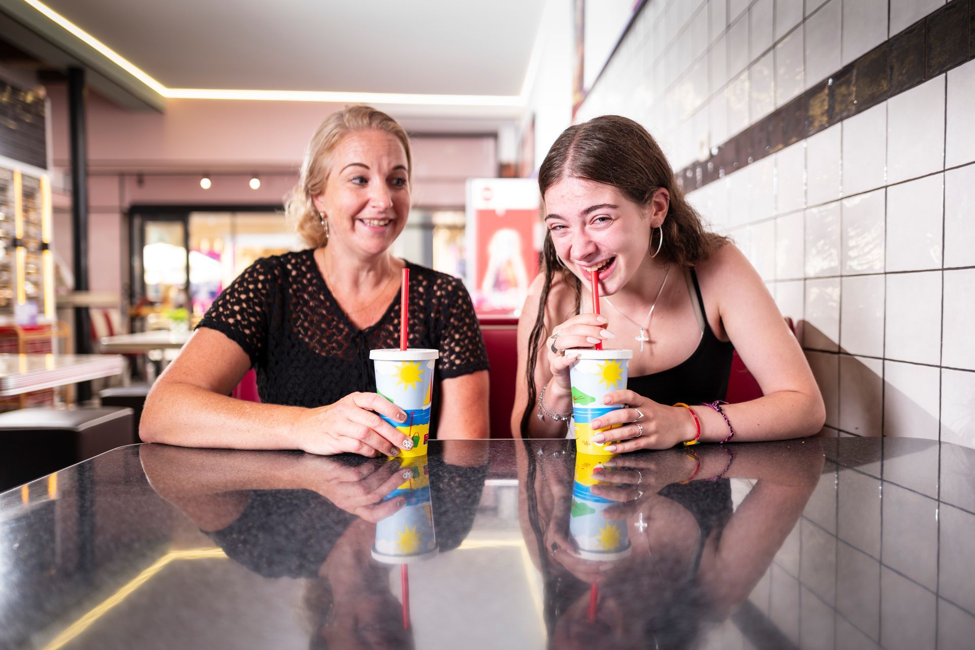 Een vrouw en een tienermeisje lachend terwijl ze frisdrank drinken in een restaurant.