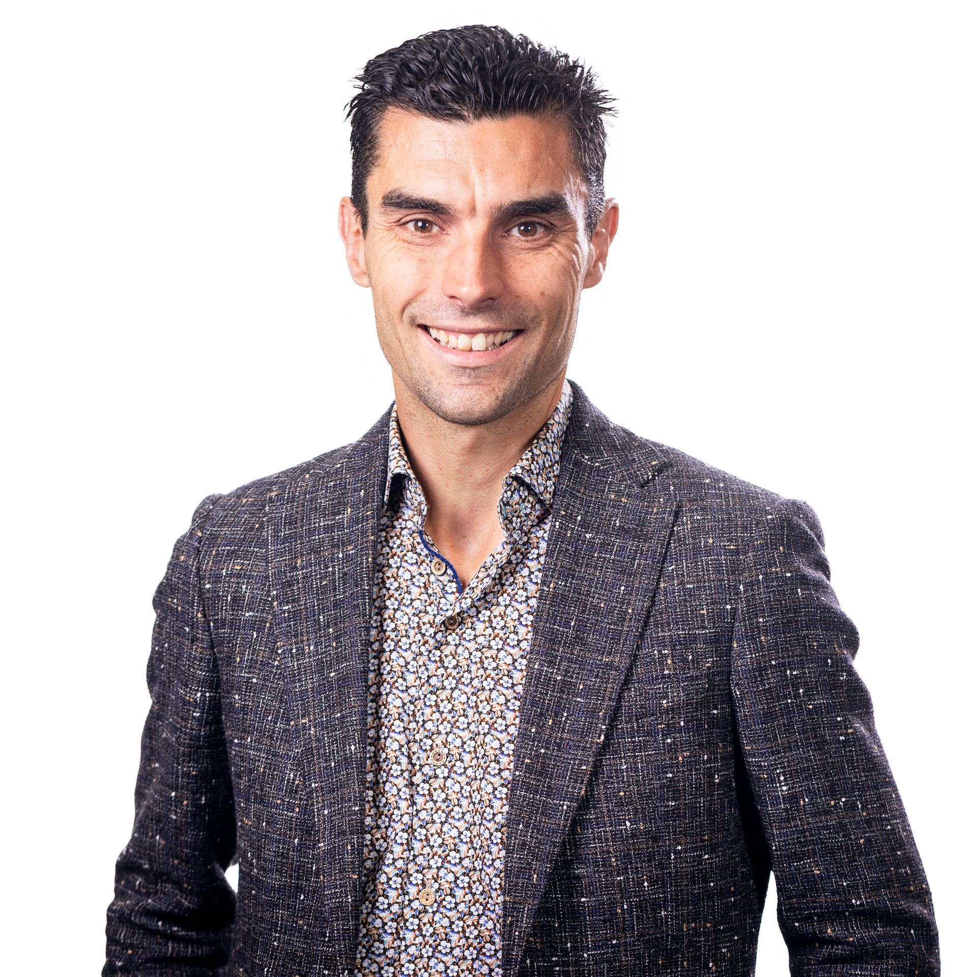 Een man lacht in een overhemd met patroon en een gespikkelde jas.