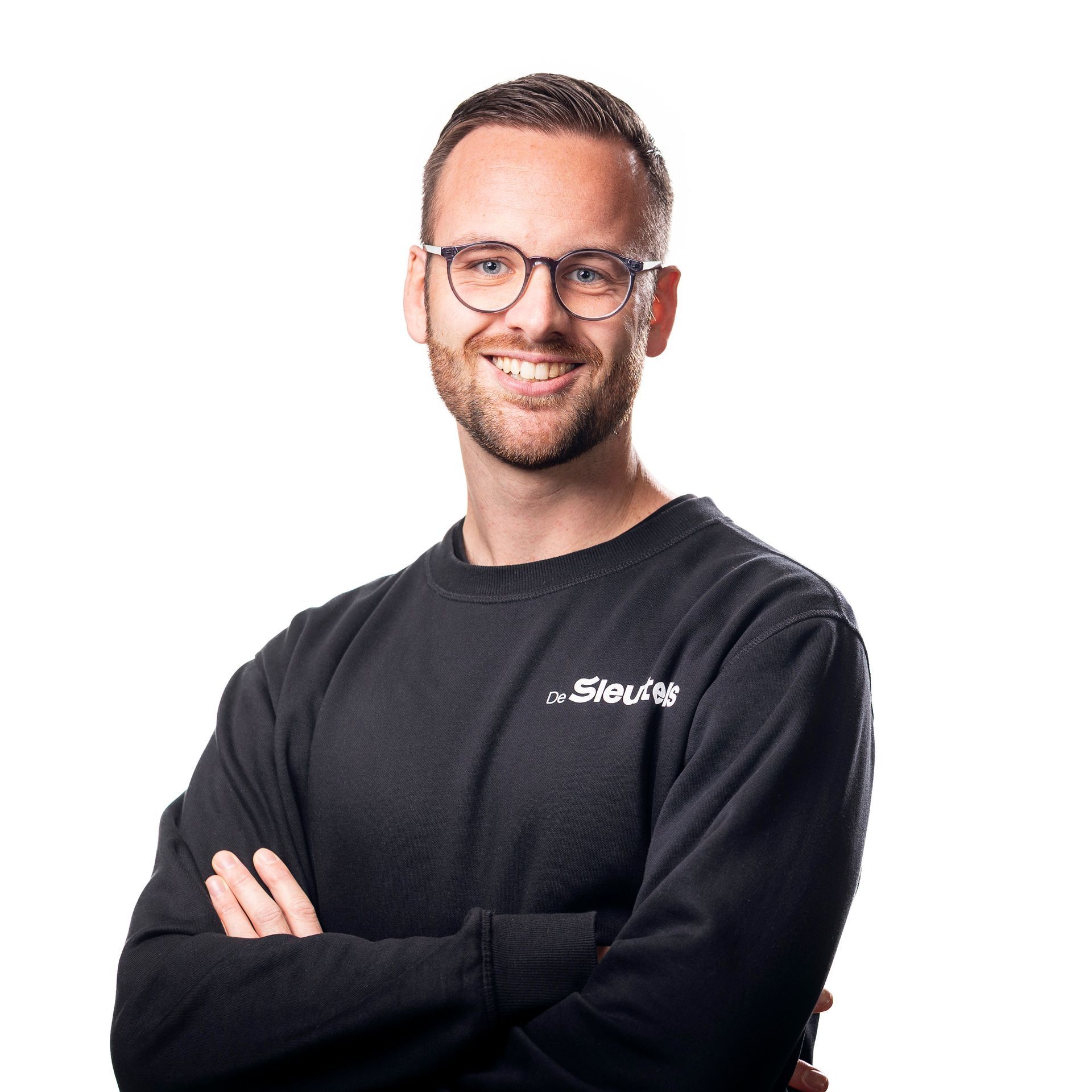 Een man met een bril en een zwarte trui aan, met de armen over elkaar, glimlacht.