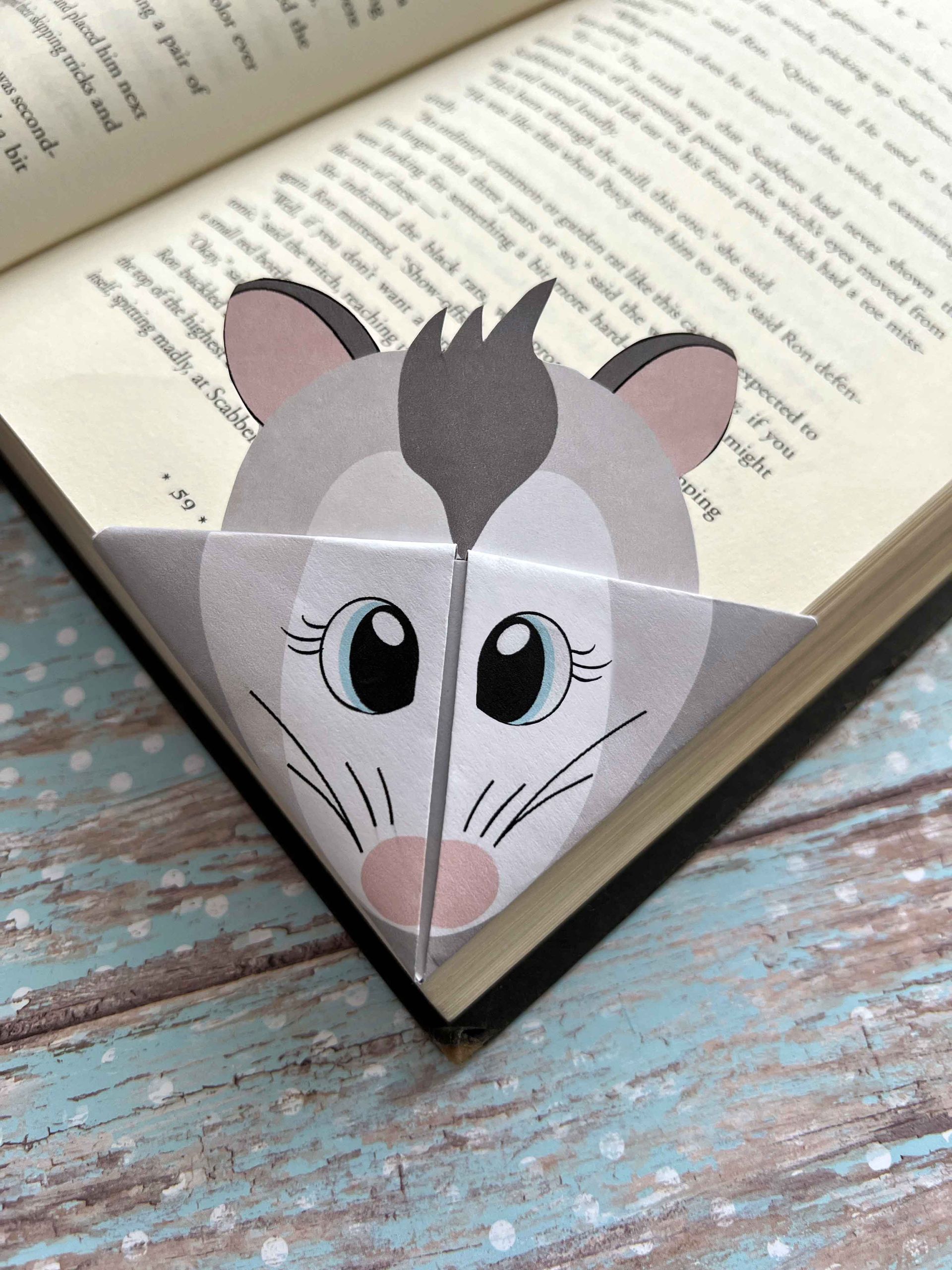 An origami bookmark of an opossum is sitting on top of an open book