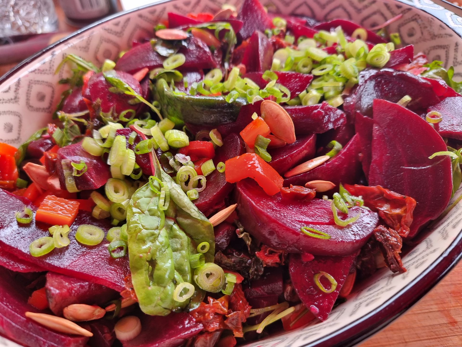 Bietensalade met fijngehakte groene uien, zaden en rode paprika in een decoratieve kom.