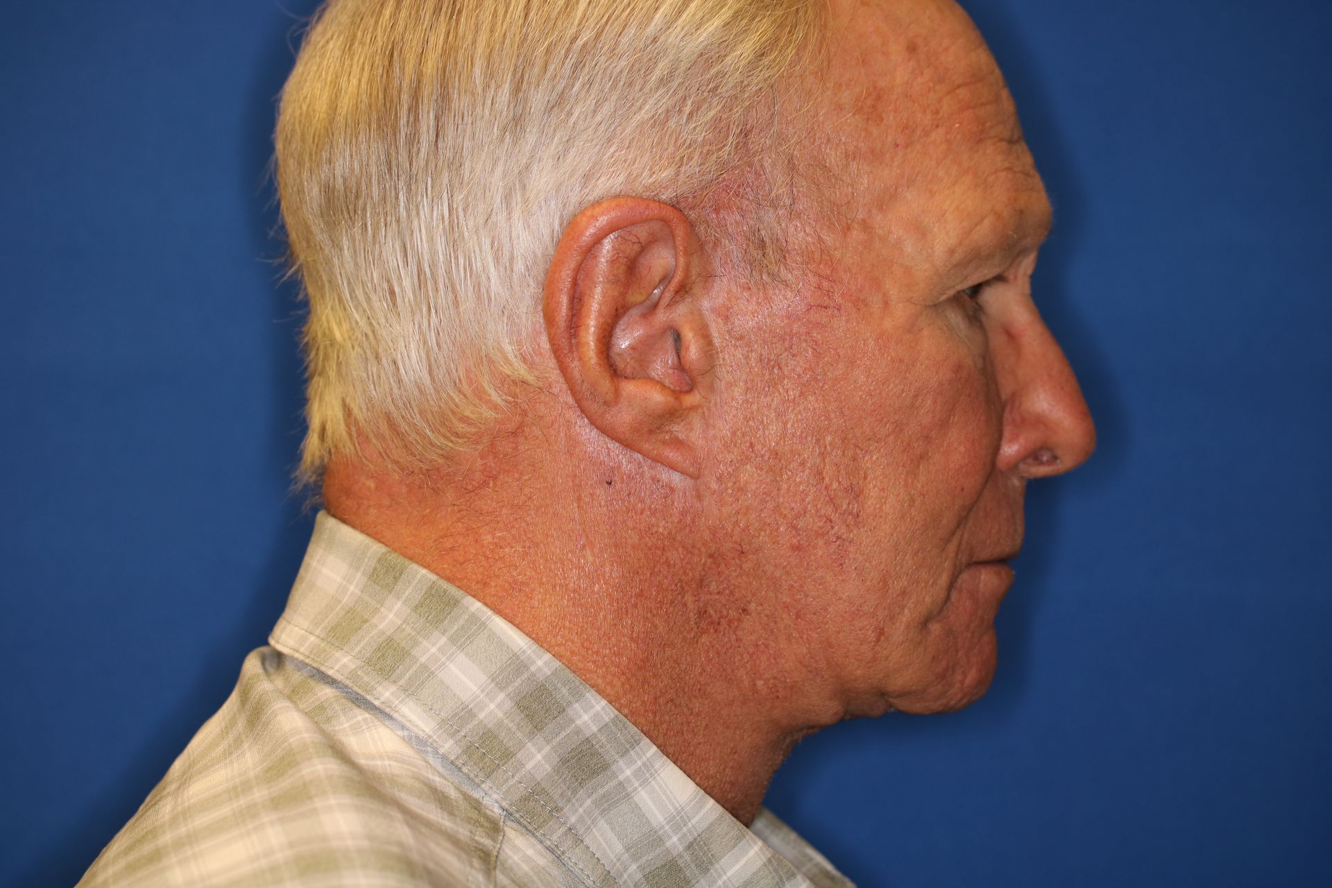 A man with gray hair and a plaid shirt is standing in front of a blue background.