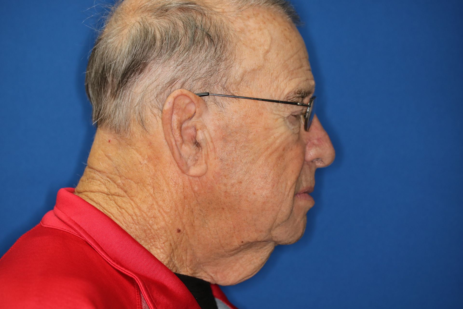 A man wearing glasses and a red shirt is standing in front of a blue background.