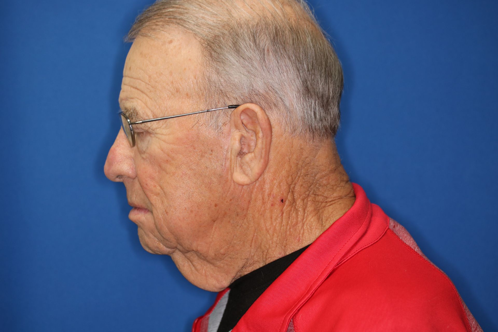 A man wearing glasses and a red shirt is standing in front of a blue background.