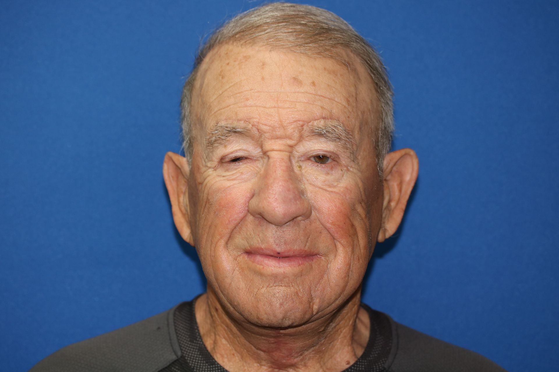 An elderly man is smiling for the camera in front of a blue background.