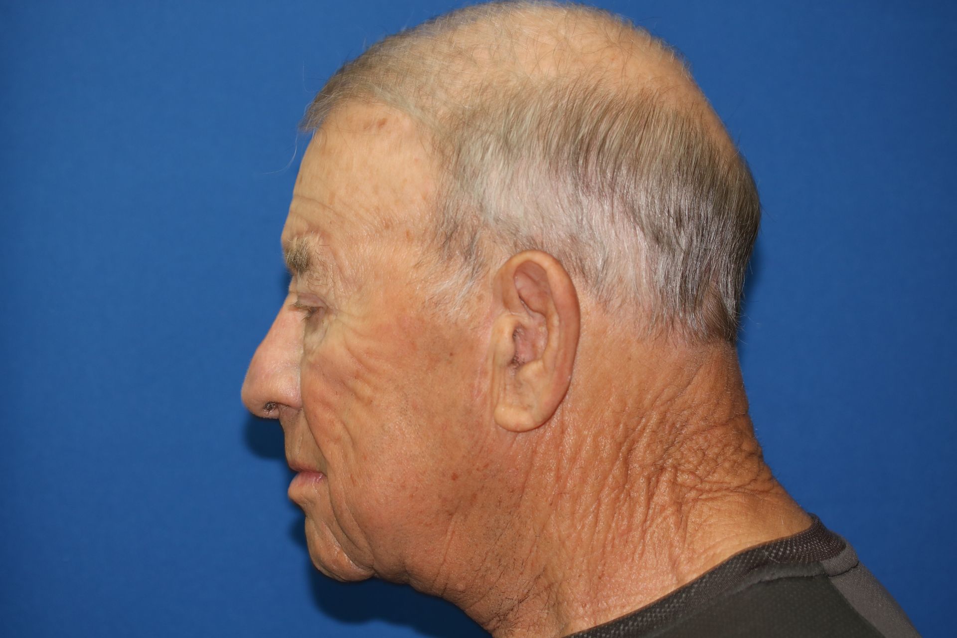 A man with gray hair is standing in front of a blue wall.