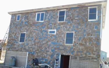 Two-story house with weathered blue shingles, several windows. Ladder leans against the side.