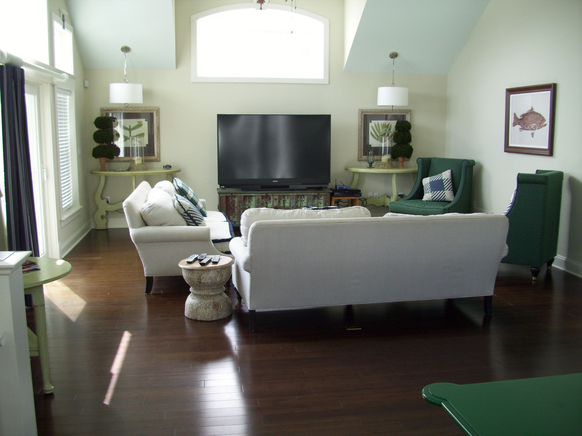 Living room with white sofas, TV, and decorative tables. Dark wood floor, light walls, and green accents.