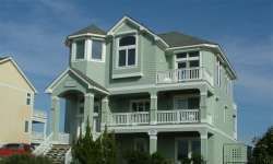 Light green three-story house with white trim, balconies, and turret under a blue sky.